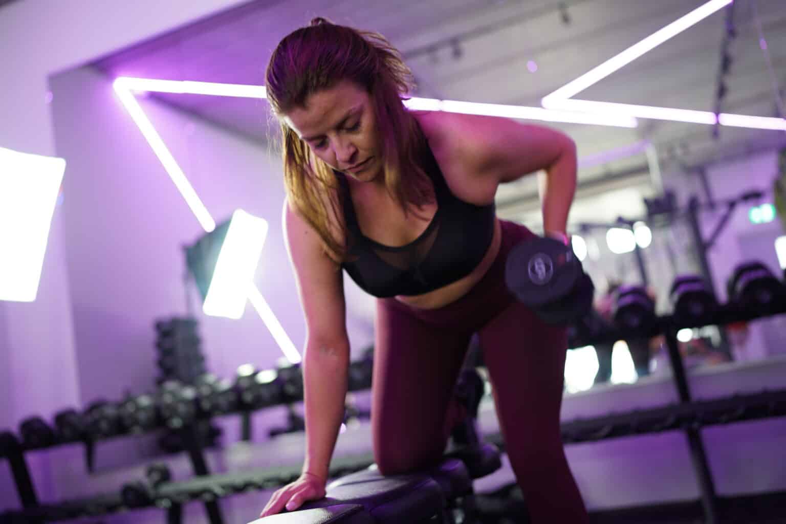 Een vrouw doet een one-arm dumbbell row met steun op een trainingsbank.